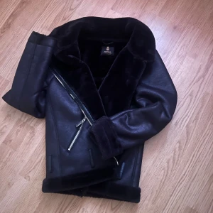 Svart skinnjacka med pälsfoder - Snygg svart skinnjacka från Bershka med mjukt pälsfoder. Jackan har en asymmetrisk dragkedja och två snedställda fickor med dragkedjor. Perfekt för kyligare dagar med sin stilrena design och varma foder.