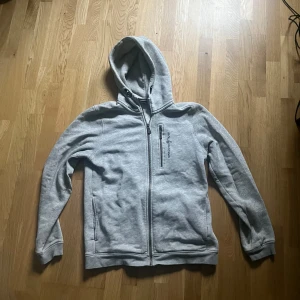 Grå hoodie från Sail Racing - Säljer en stilren grå hoodie från Sail Racing med dragkedja och broderad logga på bröstet. Perfekt för en avslappnad stil. Tveka inte att höra av er med frågor 