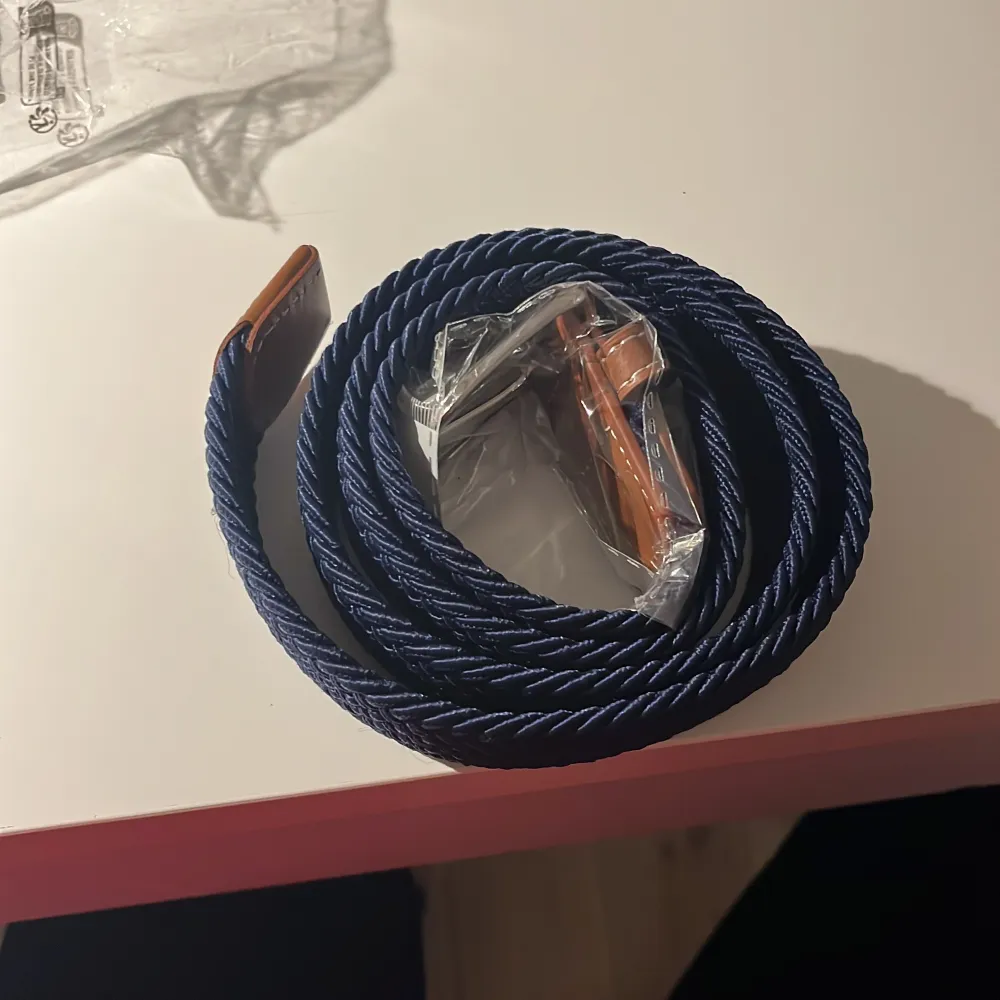 Helt nytt Snyggt blått flätat bälte med bruna skinn-detaljer. Perfekt för att ge en stilren touch till din outfit. Bältet är i ett elastiskt material som ger en bekväm passform.. Muu.