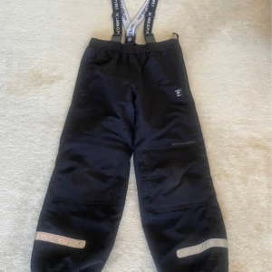 Svarta skalbyxor från Polarn O. Pyret - Svarta täckbyxor från Polarn O. Pyret med justerbara hängslen och reflexdetaljer vid benen. Perfekta för vinteraktiviteter med elastiska benslut för att hålla snön ute.