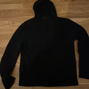 Svart kashmir hoodie från J.Crew - Säljer en svart hoodie från J.Crew i italiensk kashmir. Tröjan har en huva och knappar framtill. Perfekt för kyliga dagar när du vill ha något bekvämt och stilrent. 🖤 den har hål vid axeln och den passar inte L sitter mer som en S.