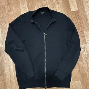 Svart tröja med dragkedja från Massimo Dutti - Säljer en stilren svart tröja från Massimo Dutti i extrafin bomull. Tröjan har en dragkedja framtill och långa ärmar, perfekt för en avslappnad look. Passar bra till både jeans och chinos.