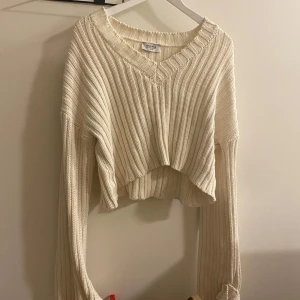 Vit ribbad croppad tröja - Säljer en superfin vit ribbad tröja från Chiquelle. Den är croppad med en snygg v-ringning och långa, vida ärmar. Perfekt för höst och vår när du vill ha något stilrent men ändå mysigt. Passar både till jeans och kjol!