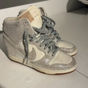 Nike sneakers med kilklack - Säljer ett par unika Nike sneakers med kilklack i grått och vitt. Har en fläck på sidan (har ej försökt tvättar bort den)