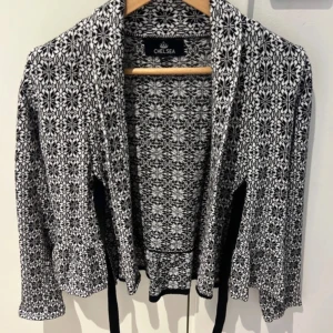 Svartvit mönstrad kofta från Chelseakofta  - Säljer en snygg svartvit kofta från Chelsea med ett unikt mönster. Perfekt för att hålla sig varm under kyliga dagar. Koftan har långa ärmar och en öppen design som gör den lätt att matcha med olika outfits. Ett måste för garderoben!