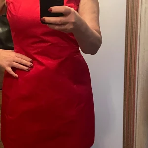 Röd klänning från Belle by Oasis - Snygg röd klänning från Belle by Oasis i storlek 36. Den har en elegant och enkel design med en tight passform som framhäver figuren. Perfekt för festliga tillfällen! Klänningen är ärmlös och har en dragkedja i ryggen för enkel påklädning.