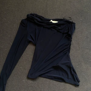 Svart oneshoulder topp från Pull&Bear - Snygg svart oneshoulder topp från Pull&Bear i storlek XS. Perfekt för en utekväll eller fest! Den har en tight passform och är tillverkad i ett mjukt och stretchigt material. Toppen har långa ärmar och en stilren design som gör den lätt att matcha med olika outfits.💙