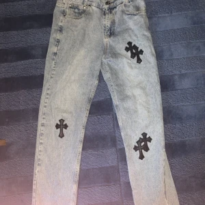 Levis 550 jeans chrome hearts - Säljer ett par Levis 550 jeans i ljusblå denim med coola svarta korsdetaljer. De har en relaxed fit och är perfekta för en avslappnad stil. Jeansen är i bra skick och har en klassisk femficksdesign. Perfekta för både vardag och fest!