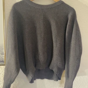 Grå stickad tröja - Mysig grå stickad tröja perfekt för kyliga dagar. Den har en avslappnad passform med långa ärmar och ribbade detaljer vid hals, ärmslut och nederkant. Perfekt för både höst och vinter!