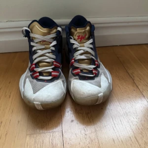 Nike Air Jordans i blått och guld - Säljer ett par Nike Air Jordans i blått och guld. Skorna har en cool design med vita och röda detaljer samt snörning. Perfekta för både vardag och sportiga aktiviteter. De är i bra skick med lite slitage på sulan.