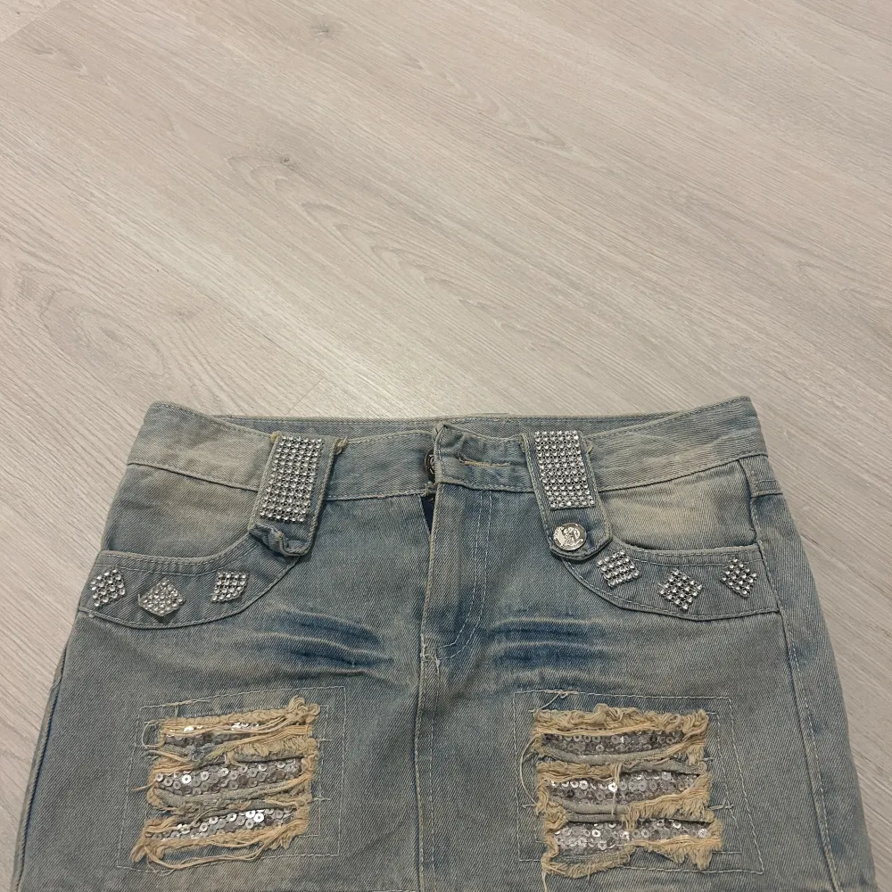 Snygg jeanskjol i storlek S, det står L men jag har storlek S och den passar mig. Coola strassdetaljer på fickorna och bältet. Kjolen har en sliten look med paljetter på de slitna delarna, vilket ger en trendig touch. Däremot så har dragkedjan gått sönder, men det går enkelt att fixa med ny dragkedja.🤗🤗. Kjolar.