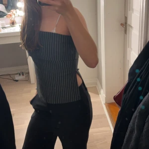 Randig tubtopp med smala axelband - Säljer en stilren randig tubtopp med smala axelband. Toppen är mörkgrå med vita ränder och har en tight passform. Perfekt för en utekväll eller fest!