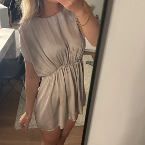 Beige kortklänning - Säljer en superfin ljus rosa kortklänning i ett mjukt och glansigt material. Säljer då den inte längre kommer till användning🥰