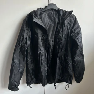 Svart vindjacka från Everest - Säljer en svart vindjacka från Everest i bra skick. Jackan har en huva och dragkedja framtill, perfekt för blåsiga dagar. Den är lätt och smidig att ha med sig, och passar bra till både vardag och friluftsliv. Storlek 36