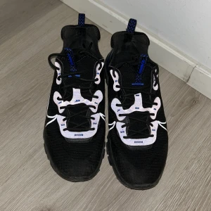 Nike vision react blå - Säljer ett par svarta Nike vision react sneakers i mycket bra skick. De har snygga blå detaljer och vit snörning. Perfekta för både träning och vardag. Skorna har en modern design med bekväm passform och är gjorda i syntetmaterial.