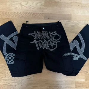 Two minus - Säljer ett par svarta byxor med coolt grafiskt tryck i vitt. Byxorna har en loose passform och är perfekta för en avslappnad stil. De har praktiska fickor och trycket ger en unik touch. Perfekta för dig som vill sticka ut!