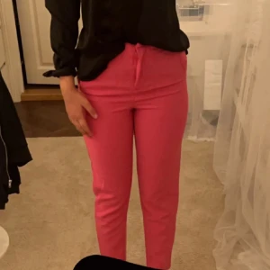 Rosa byxor - Säljer ett par snygga rosa byxor i normal passform. De är perfekta för både vardag och fest med sin fräscha färg. Byxorna har en enkel design med knytning i midjan för en bekväm passform.