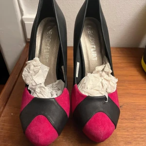 Svart och rosa pumps från Bodyflirt - Snygga pumps i svart och rosa från Bodyflirt. De har en spetsig tå och hög klack, vilket ger en elegant look. Skorna är i syntetmaterial och har en cool färgkombination som verkligen sticker ut. Perfekta för festliga tillfällen när du vill göra ett intryck!