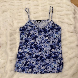 Blå blommig linnetopp - Säljer en superfin blå blommig linnetopp med smala axelband. Toppen har ett vackert mönster i olika blå nyanser och är perfekt för sommardagar. Materialet känns lätt och luftigt, vilket gör den idealisk för varma väder. Passar perfekt till både jeans och kjol!