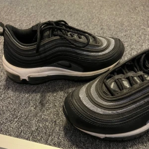 Nike Air Max sneakers i svart och silver - Säljer ett par snygga Nike Air Max sneakers i svart och silver. De har en cool vågig design med snörning och en bekväm sula. Perfekta för både vardag och träning. Använda men i bra skick!