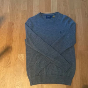 Ralph Lauren stickad tröja - Säljer en grå stickad crewneck tröja från Polo Ralph Lauren i merinoull. Köpt på NK för ca 1600, har använt tröjan några enstaka gånger och det är inga defekter alls. Pris går att diskutera!