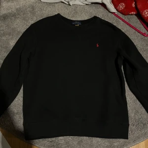 Svart tröja från Polo Ralph Lauren - Säljer en klassisk svart tröja från Polo Ralph Lauren i storlek 14-16 storlek xs i herr storlek. Tröjan har en enkel design med en liten röd logga på bröstet. Perfekt för både vardag och lite finare tillfällen. Den är i mycket bra skick och superbekväm att ha på sig. Passar perfekt till höst och vinter!