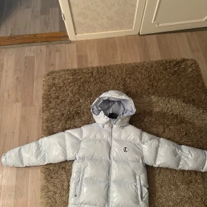 Lukamachain pufferjacka - baby blå  - Säljer en helt ny och superfin baby blå pufferjacka med huva från lukamachain. Jackan har en cool logga på bröstet och en stor stjärndetalj på ryggen. Jackan är perfekt för vintern och är även vattentät!