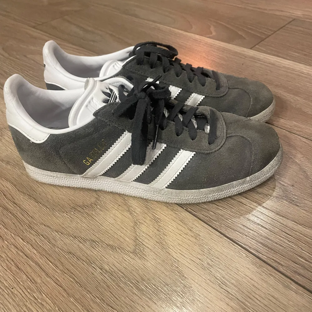 Säljer ett par grå Adidas Gazelle sneakers i mycket bra skick. De har den klassiska designen med vita ränder och snörning. Skorna är gjorda i mocka och har en vit sula. Perfekta för vardagsbruk och ger en stilren look. Skorna är använda några gånger🙏🏼💕. Skor.