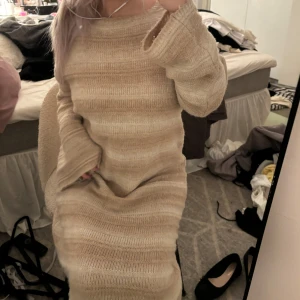 Beige stickad långklänning - Mysig beige stickad långklänning perfekt för kyliga dagar. Den har en loose passform med långa ärmar och en rund halsringning. Klänningen är i ett mjukt material som känns skönt mot huden. Perfekt för höst och vinter!
