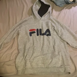 Grå hoodie från FILA - Säljer en snygg och bekväm grå hoodie från FILA. Perfekt för både vardag och chill. Den har en klassisk design med FILA-loggan i rött och blått på bröstet. Passar perfekt för höst och vår. Passar även för dom som är 160cm