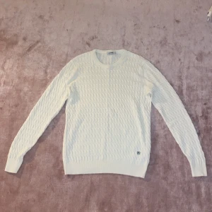 Vit stickad tröja - Säljer en stilren vit stickad tröja med kabelstickat mönster. Perfekt för kyliga dagar och passar både till vardags och lite finare tillfällen. Tröjan har långa ärmar och en rund halsringning. Supermysig och lätt att matcha med andra plagg!