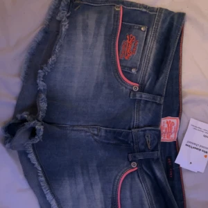 Blå jeansshorts från Superdry - Säljer ett par snygga blå jeansshorts från Superdry i mycket bra skick. De har fransiga kanter och coola röda detaljer vid fickorna. Perfekta för sommaren och festivaler! 🕶️skriv för mått!