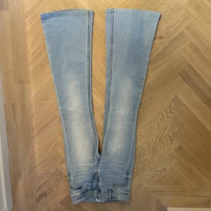 Ljusblå bootcut jeans - Säljer ett par ljusblå bootcut jeans i bra skick. De har en snygg tvättad look och är perfekta för både vardag och fest. Jeansen har en klassisk design med knappar och dragkedja framtill. Passar perfekt till en avslappnad stil eller med klackar för en mer uppklädd look.
