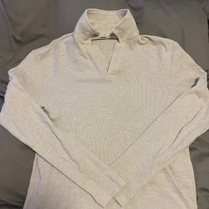 Beige långärmad tröja från East West - Säljer en stilren beige långärmad tröja från East West. Perfekt för både vardag och lite finare tillfällen. Tröjan har en klassisk krage och är i ett mjukt material som känns skönt mot huden. Passar perfekt till höst och vår!