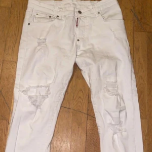 Vita jeans från Dsquared2 - Säljer ett par vita jeans från Dsquared2 i storlek 48. De har en cool distressed look med slitningar på benen och en knappgylf. Perfekta för en avslappnad men stilren outfit. Tillverkade i Italien.