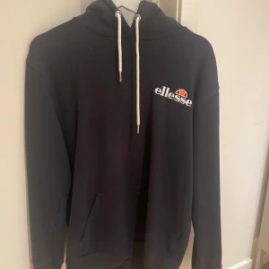 Mörk blå hoodie från Ellesse - Säljer en snygg mörk blå  hoodie från Ellesse i bra skick. Den har en klassisk design med vit dragsko och logga på bröstet. Perfekt för både chill och träning. Stor ficka fram för att hålla händerna varma eller förvara småsaker. Skön och stilren, passar till det mesta! 🖤