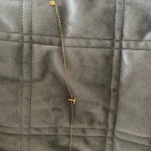 Guldhalsband med T - Säljer edblad armband i guld med T. Köpt i sommras, använd fåtal gånger. Längden är justerbar med en liten förlängningskedja. 