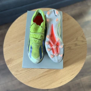 Adidas x crazyfast elite ag 41/13 - Säljer ett par grymma gröna fotbollsskor från Nike. De har en cool design med blå och vita detaljer och en ljusorange sula med dobbar för bästa grepp på planen. Perfekta för fotbollsträning eller match! Skorna har snörning för en tight passform.