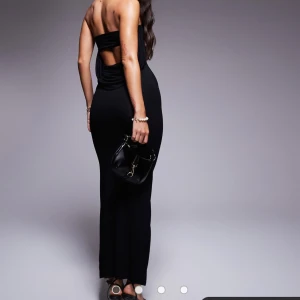 Svart långklänning med öppen rygg - Säljer en elegant svart lång tubklänning med en stilren öppen rygg. Perfekt för festliga tillfällen. Klänningen har en tight passform som framhäver figuren och är tillverkad i ett mjukt och bekvämt material. Ett måste för garderoben! Den är helt oanvänd med prislappen kvar!