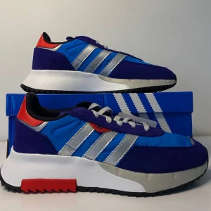 Adidas Retropy F2 Sneakers - Snygga Adidas Retropy F2 sneakers i blått och lila med silverdetaljer. Skorna har en modern design med klassiska ränder och röd accent på hälen. Perfekta för både vardag och träning. Helt nya i kartong!