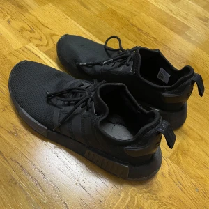 Svarta Adidas NMD sneakers - Säljer ett par svarta Adidas NMD sneakers i bra skick. De funkar till väldigt mycket, lätta att bära på, ett par skor man it kan gå fel med. Säljer för bra pris.