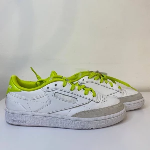 Reebok Club C85 - Säljer ett par snygga vita sneakers från Reebok med limegröna detaljer och snörning. Skorna har en klassisk design med en touch av färg som gör dem unika. Perfekta för vardagsbruk och ger en fräsch look till din outfit. De är i bra skick och redo för nya äventyr!