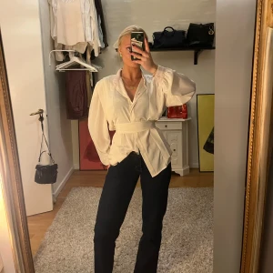 Vit blus med knytband - Säljer en stilren vit blus med knytband i midjan. Blusen har långa ärmar och en v-ringad design. Perfekt för både vardag och festliga tillfällen. Passar bra till jeans eller kjol för en chic look.