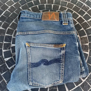 Blå jeans från Nudie Jeans - Säljer ett par snygga blå jeans från Nudie Jeans i storlek W31 L32. Modellen heter tape Ted sitter slim. Passar mig som är 180 cm perfekt. Det finns en liten fläck som man kan se på sista bilden, men syns knappt och kan säkert tvättas bort. Pris kan diskuteras vid snabb affär, skriv om ni har fler frågor!🙌