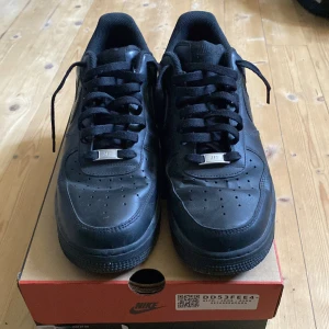 Svarta Nike Air Force 1 - Säljer ett par klassiska svarta Nike Air Force 1 i bra skick. Skorna har en stilren design med snörning och är perfekta för både vardag och fest. De är i storlek herr 45 och kommer i originalkartong. Perfekta för dig som vill ha en tidlös sneaker i garderoben!
