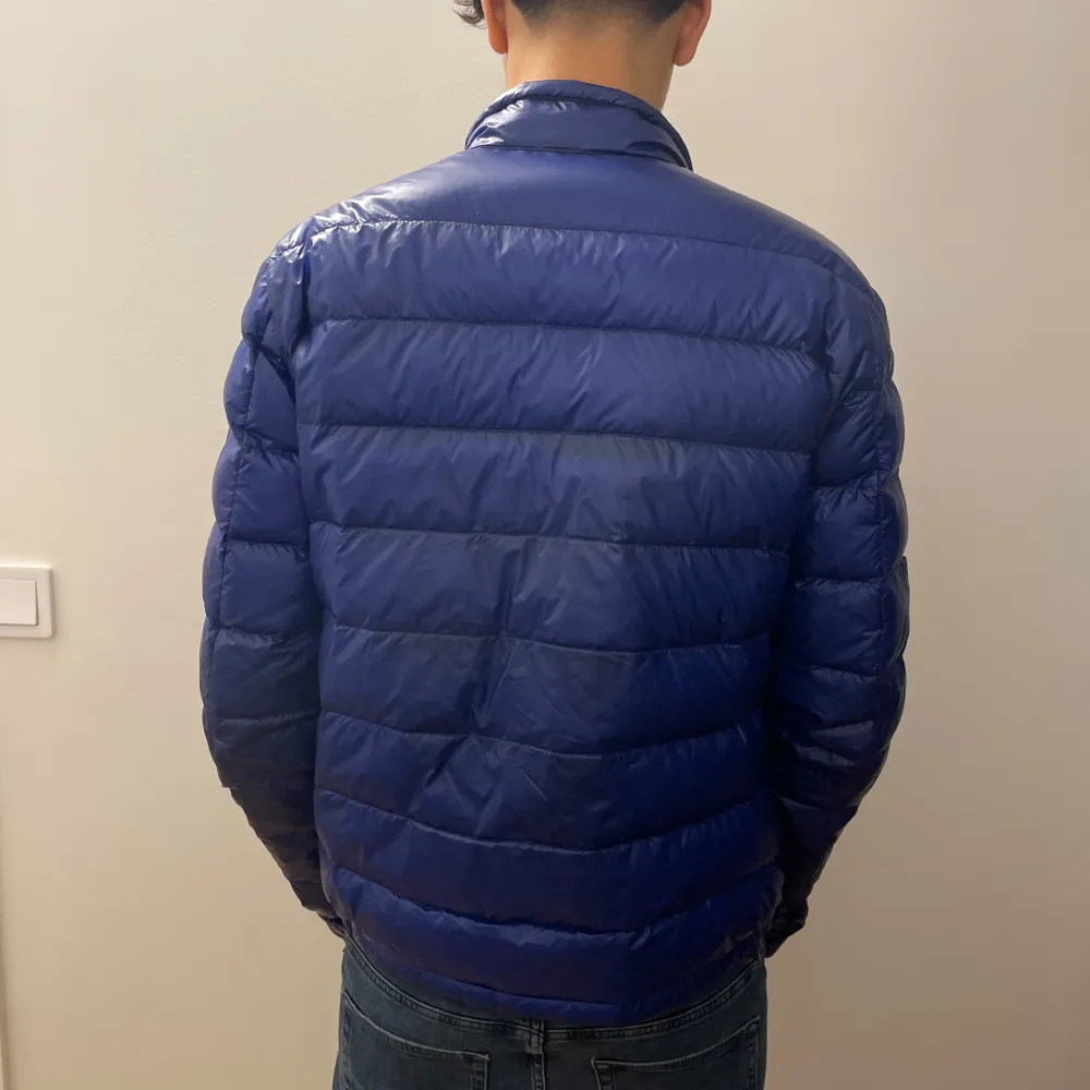 Säljer en snygg blå dunjacka från Moncler i mycket bra skick. Jackan har en quiltad design med dragkedja framtill och en liten logga på ärmen. Perfekt för höst och vår, och den är både stilren och varm. Passar perfekt till jeans för en casual look. Original pris 11 890 kr. Jackor.