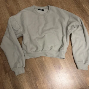 Beige croppad sweatshirt från BikBok - Säljer en stilren beige croppad sweatshirt från BikBok. Tröjan har långa ärmar och en rund halsringning, perfekt för en avslappnad look. Passar bra till jeans eller leggings.