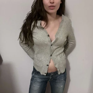 Grå kofta med knappar 100% Kashmir Marc Jacobs - Säljer en grå kofta med knappar framtill. Koftan har en enkel design med långa ärmar och ribbade muddar. Perfekt för en avslappnad stil. har ett litet hål