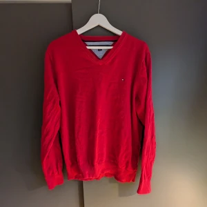 Röd v-ringad tröja från Tommy Hilfiger - Snygg röd v-ringad tröja från Tommy Hilfiger. Perfekt för en stilren look med långa ärmar och ribbade kanter. En klassisk design som funkar till många tillfällen.
