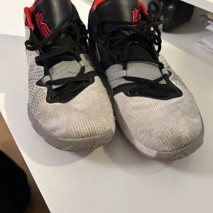 Nike kyries flytrap  - Snygga Nike sneakers med svart och röd detalj. Skorna har en vit bas med svarta snören och en röd insida. Perfekta för en sportig look med en bekväm passform.